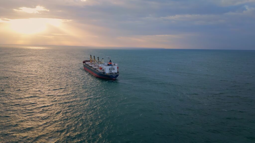 Bulk carrier ship sailing to sunset. Drone view vessel floating in dark ocean.