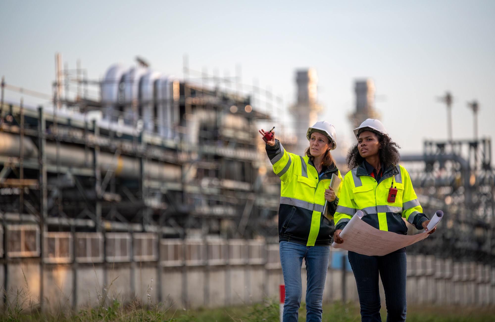 Engineers wearing safety gear, including hard hats examining survey a large blueprint tablet standin